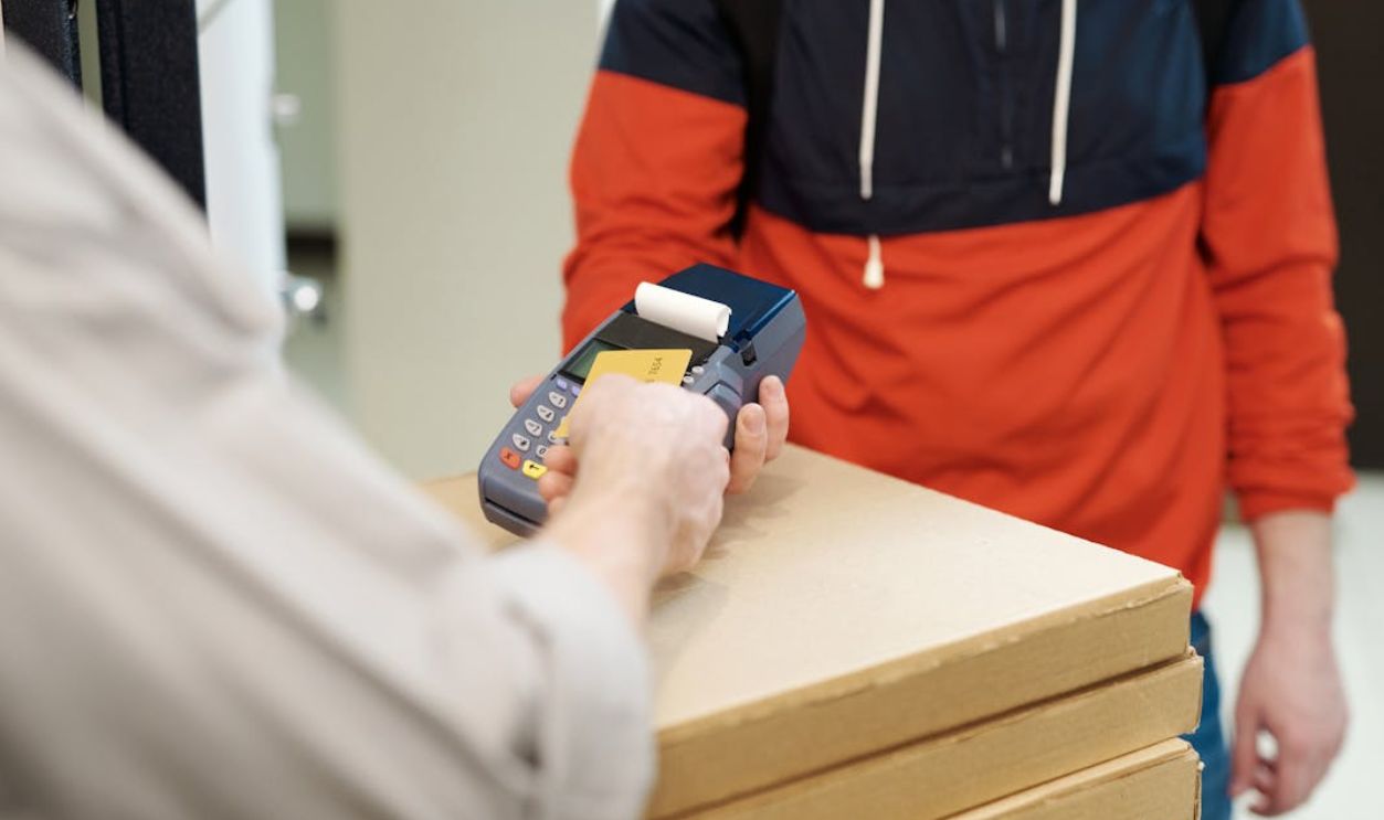 Customer making a contactless payment to a delivery person with a card reader and pizza boxes
