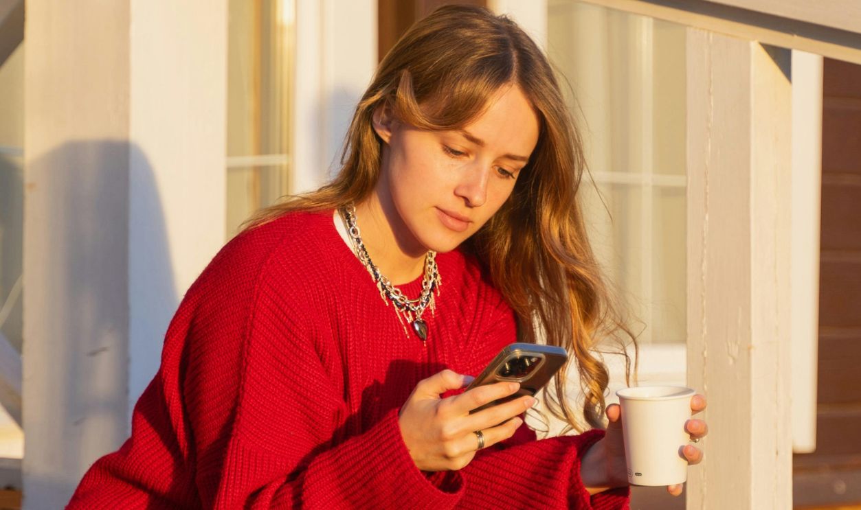 A woman in a red sweater and sneakers sits on wooden stairs, enjoying sunset light
