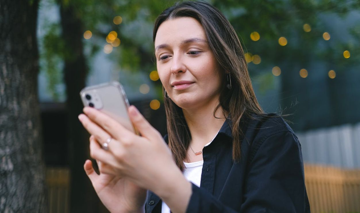 A young woman looking at her smartphone with a gentle smile in an outdoor setting, surrounded by nature