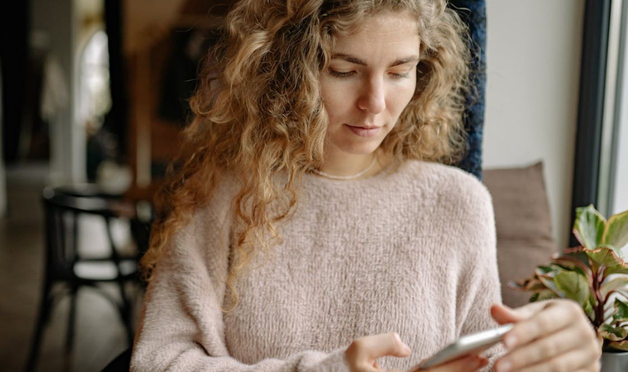A woman in a cozy sweater using a smartphone in a relaxed indoor environment