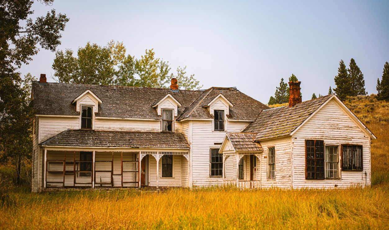 An old abandoned house surrounded by an overgrown grassy field, showcasing rustic charm