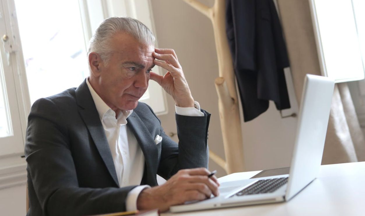 Senior businessman in office pondering work issues on laptop, showing stress.