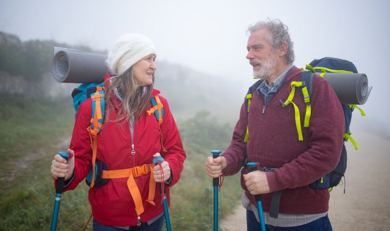 A senior couple hiking with trekking poles amidst foggy mountain landscape in Portugal, sharing a joyful moment.