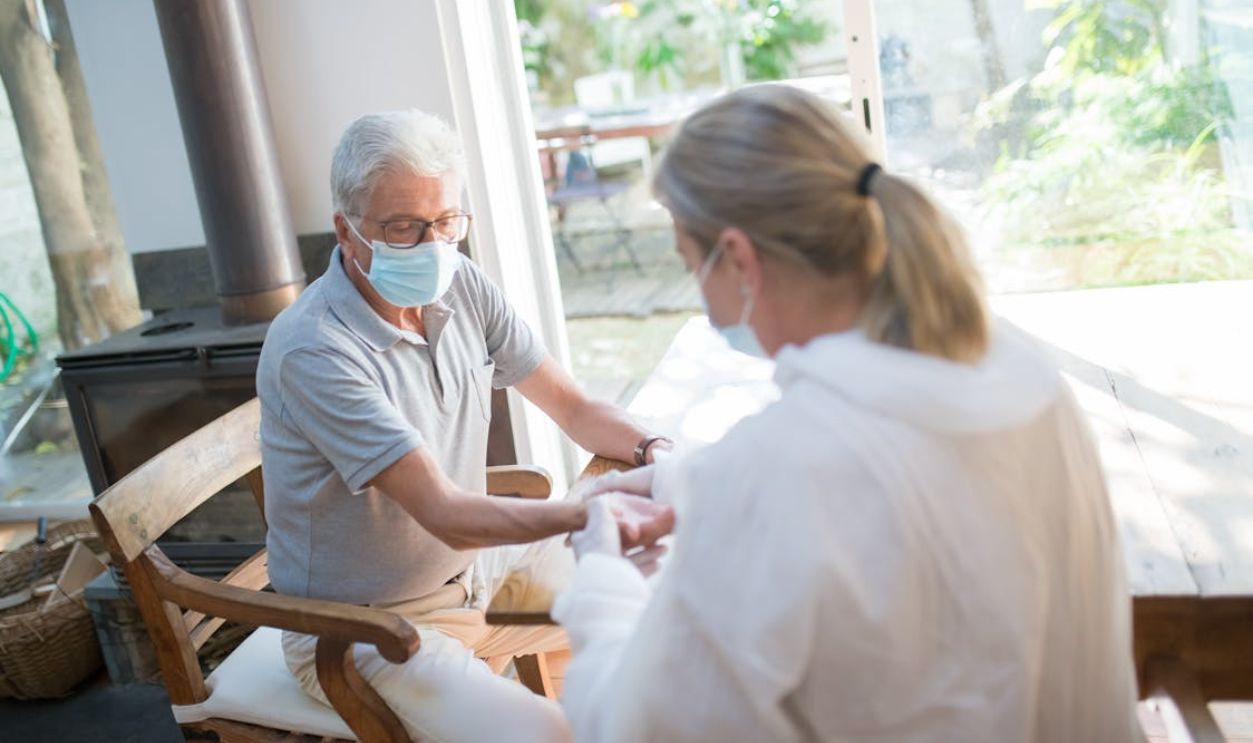 A healthcare worker examining a senior man at home with face masks during the pandemic.