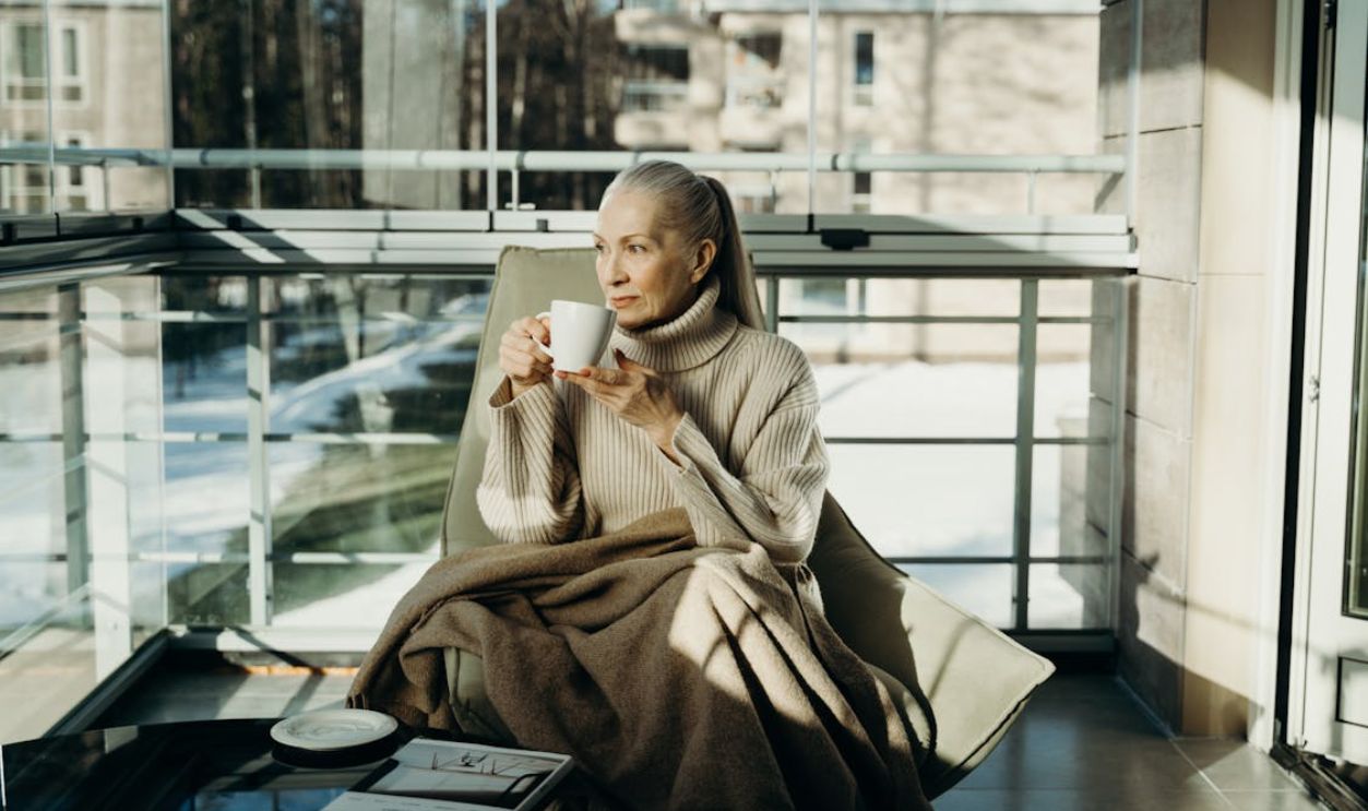 Senior woman enjoys a peaceful moment with a cup of coffee in a sunlit indoor space.