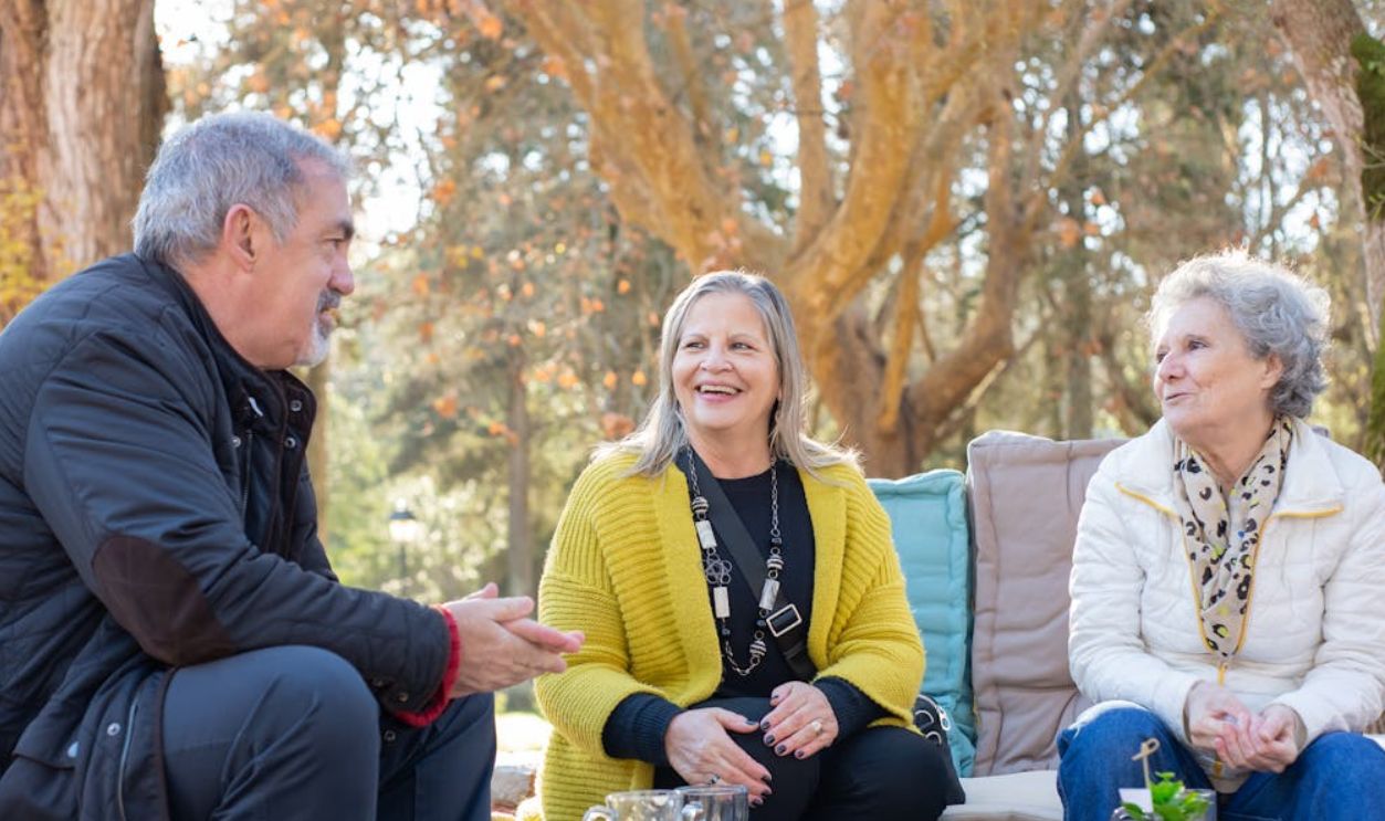 Three senior adults enjoying tea outdoors on a wooden table in Portugal's forest park.