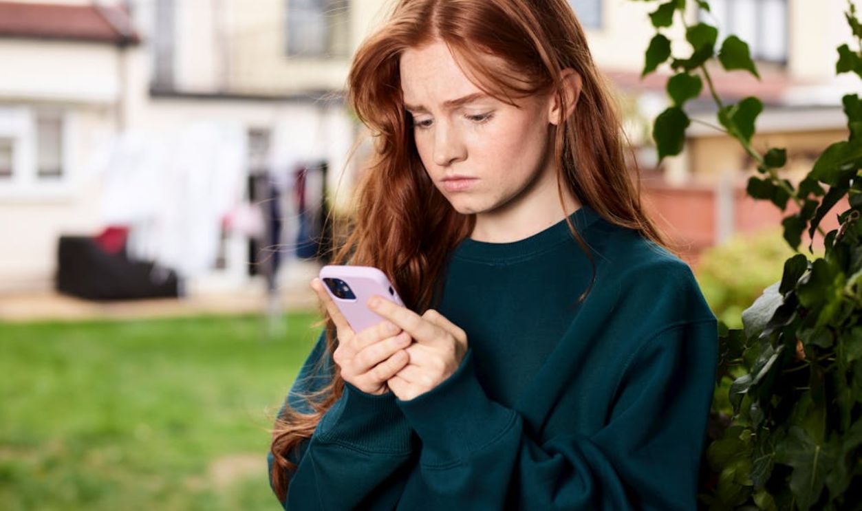 Teen girl with red hair looking at phone outdoors in a courtyard