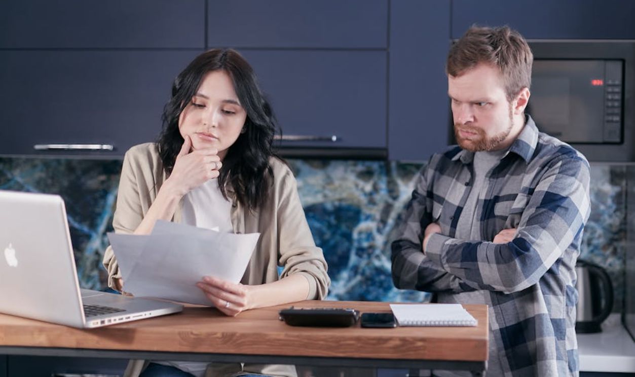 A couple sitting at a kitchen desk reviewing financial documents, using a laptop