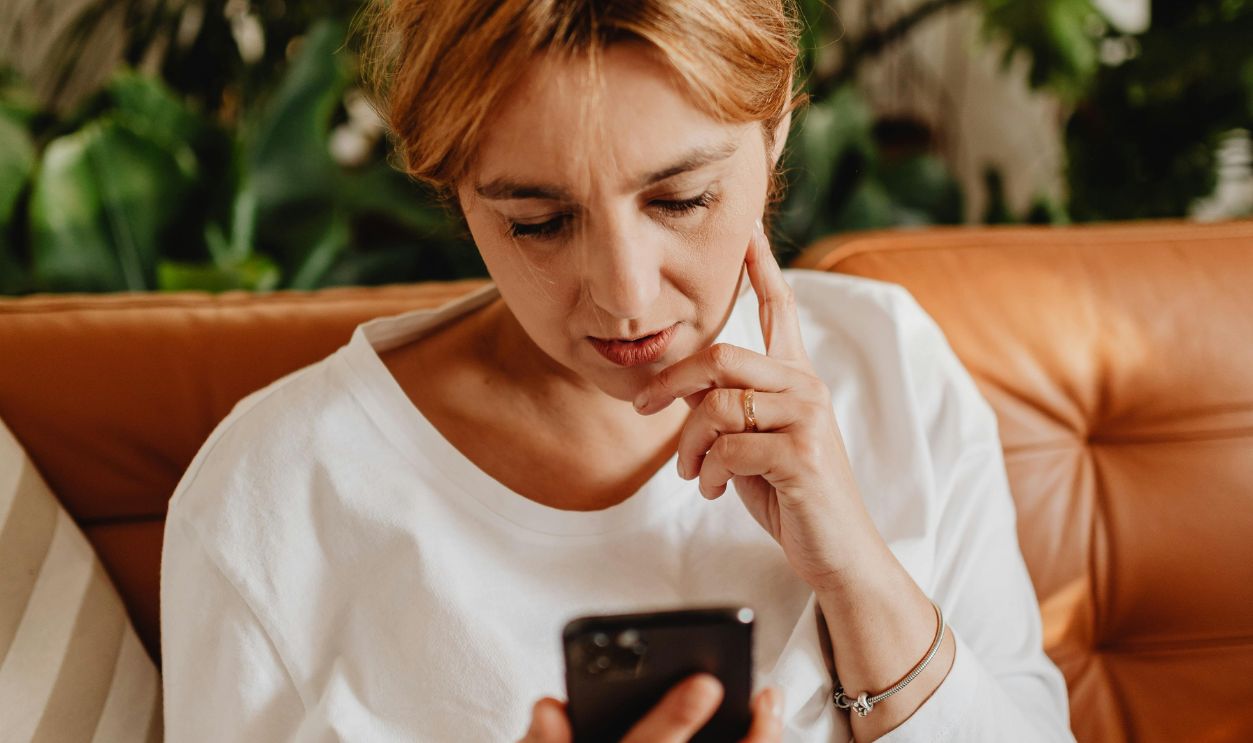 Woman sitting on couch using smartphone, surrounded by plants indoors