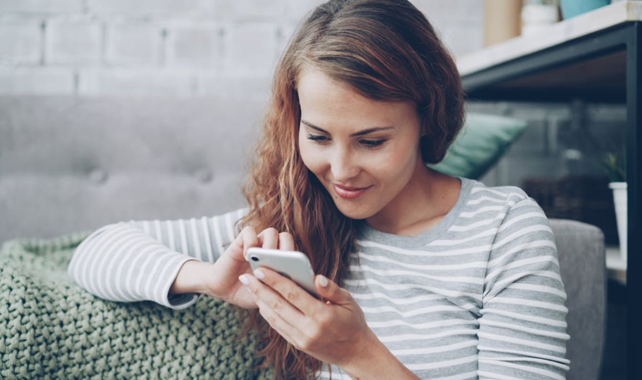 Young woman in casual attire using smartphone, sitting indoors comfortably