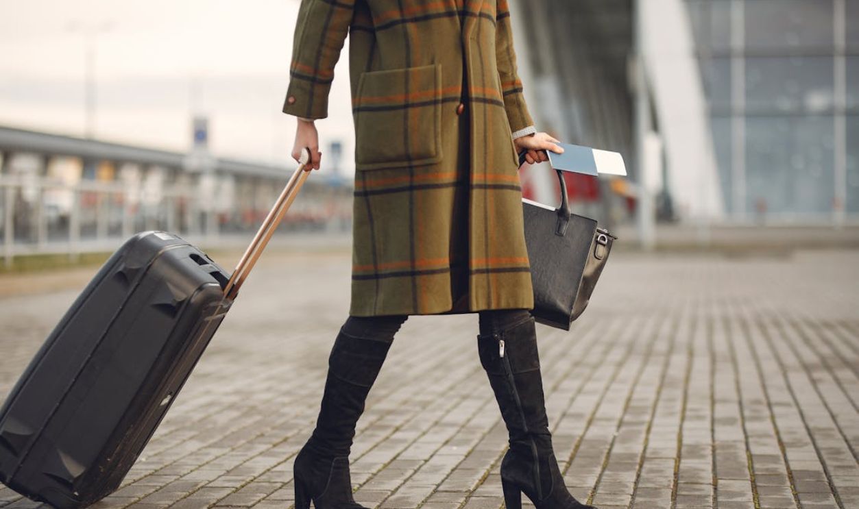 Stylish woman pulls suitcase at airport, ready for travel