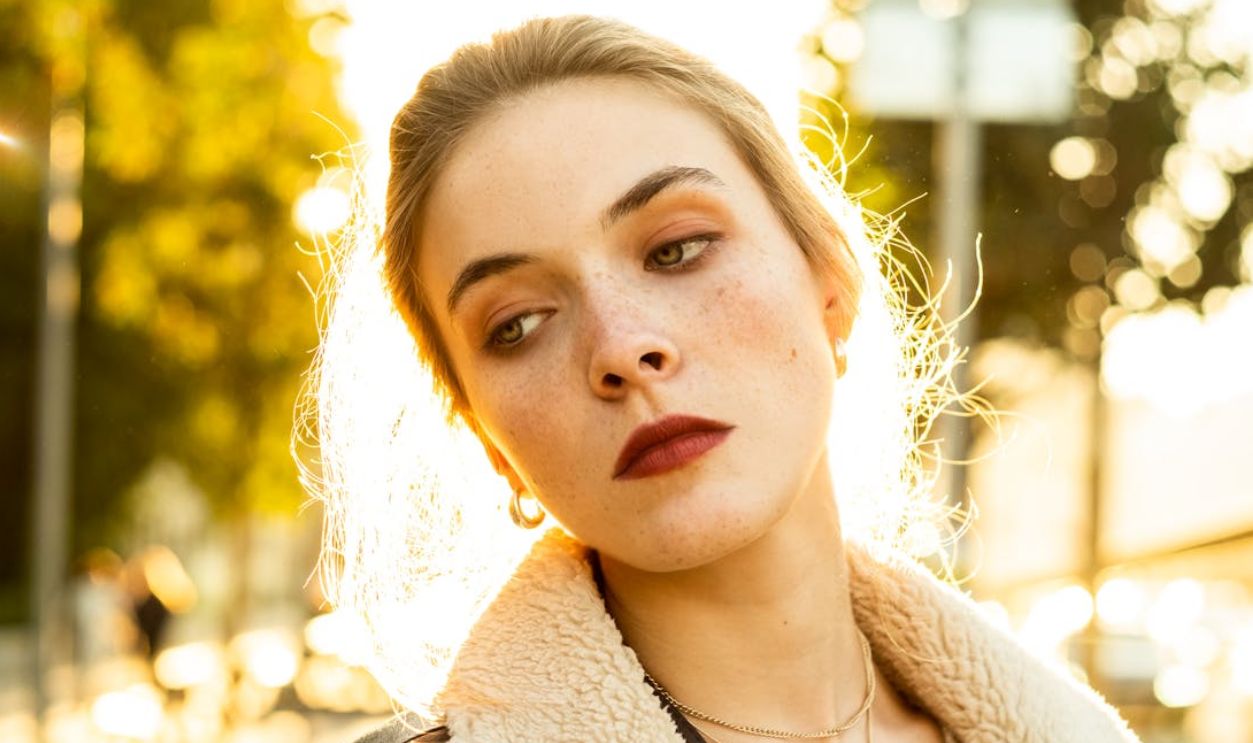 A young woman with blonde hair poses outdoors in warm autumn light