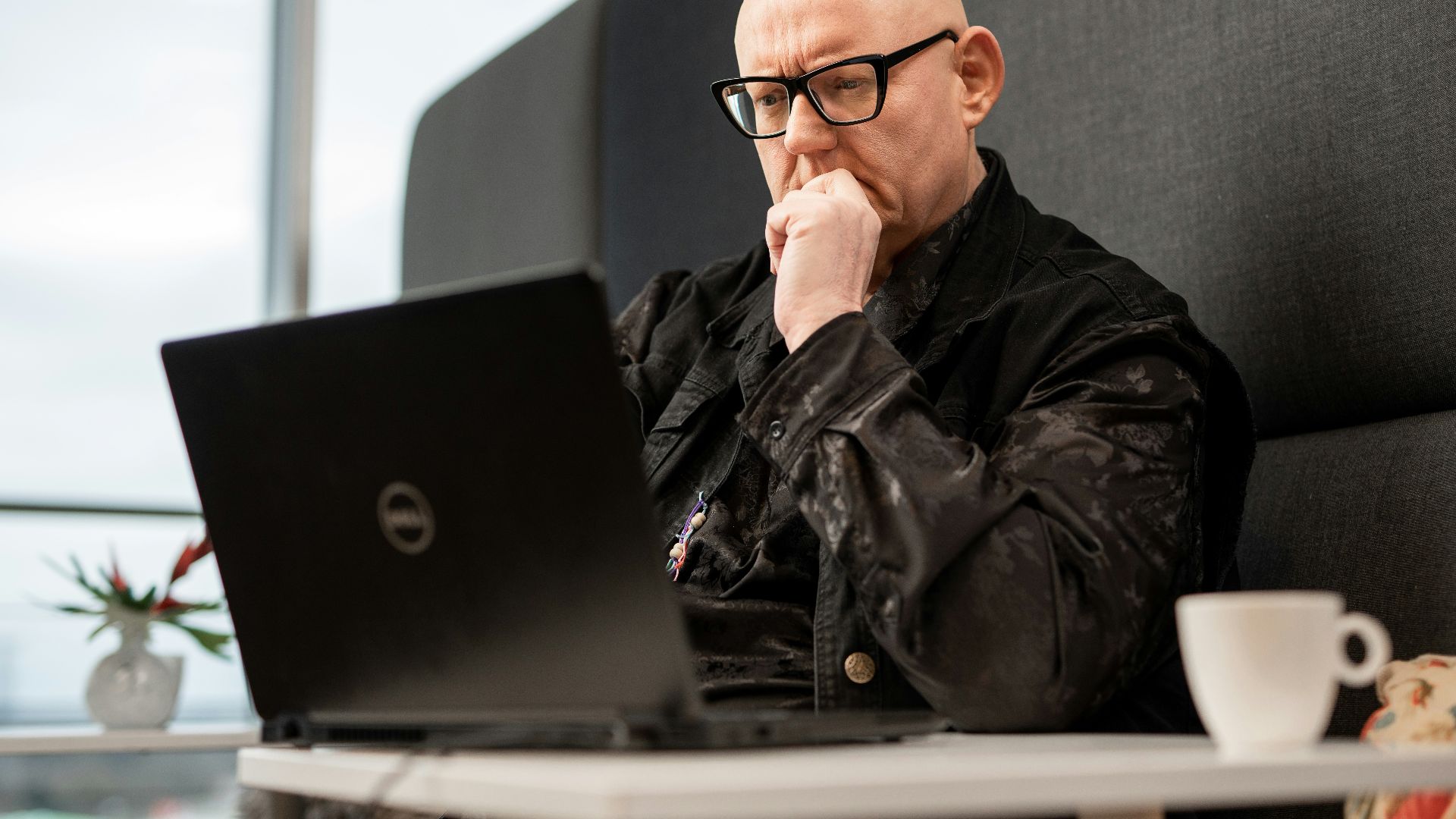 a bald man sitting in front of a laptop computer