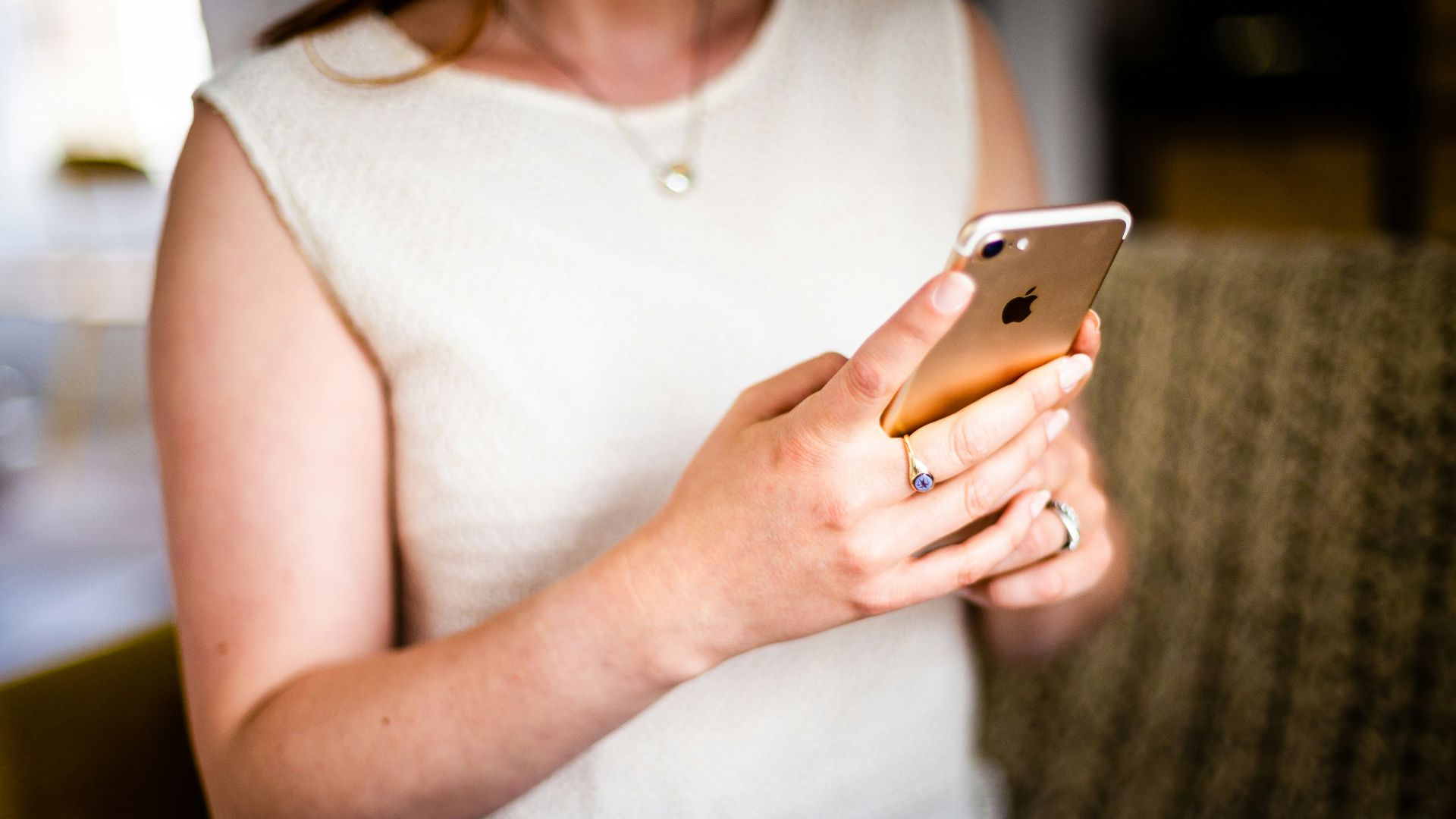 shallow focus photo of person in white sleeveless shirt holding gold iPhone 7