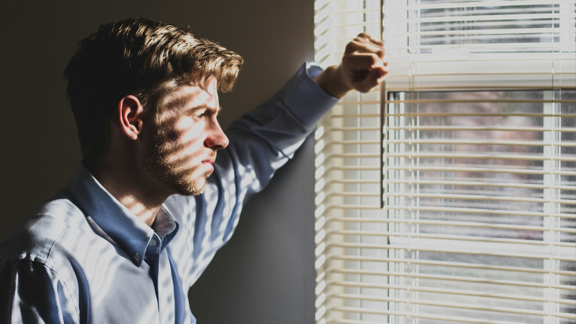 person near clear glass window pane and window blinds low-light photography