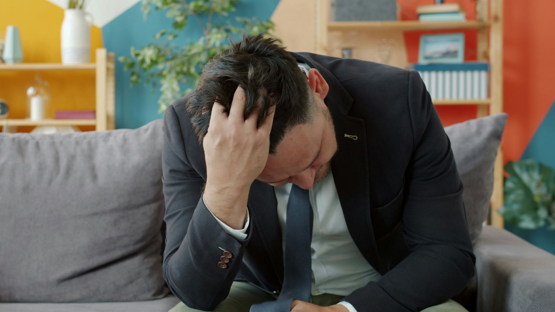 Man in suit sitting on couch with head in hands.