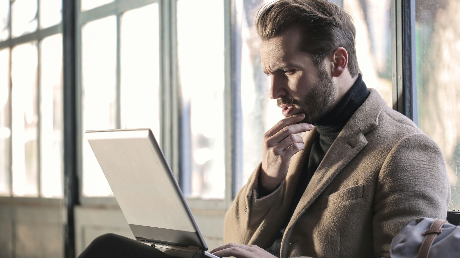 man holding his chin facing laptop computer