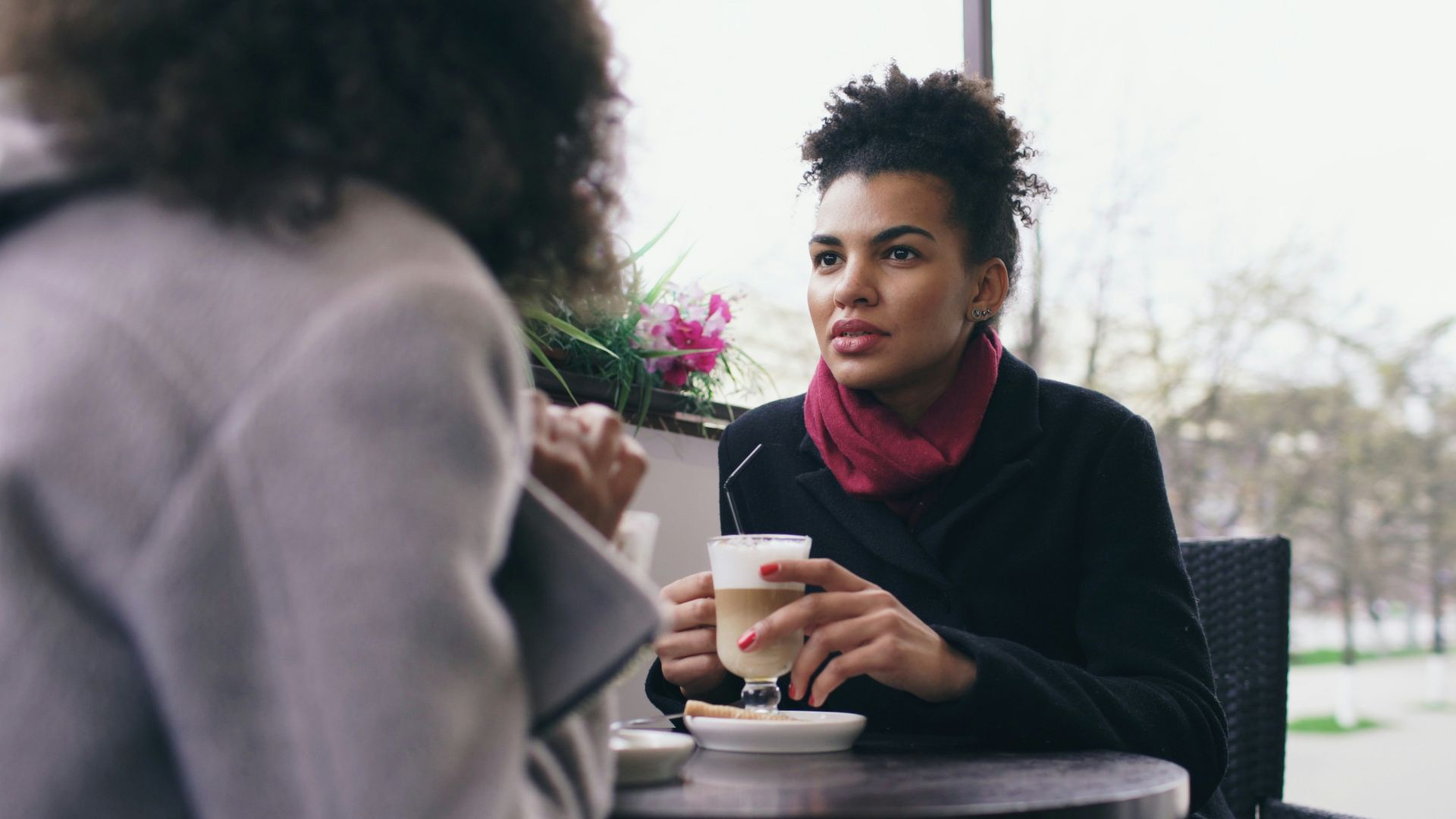 Two women talking at an outdoor cafe table.