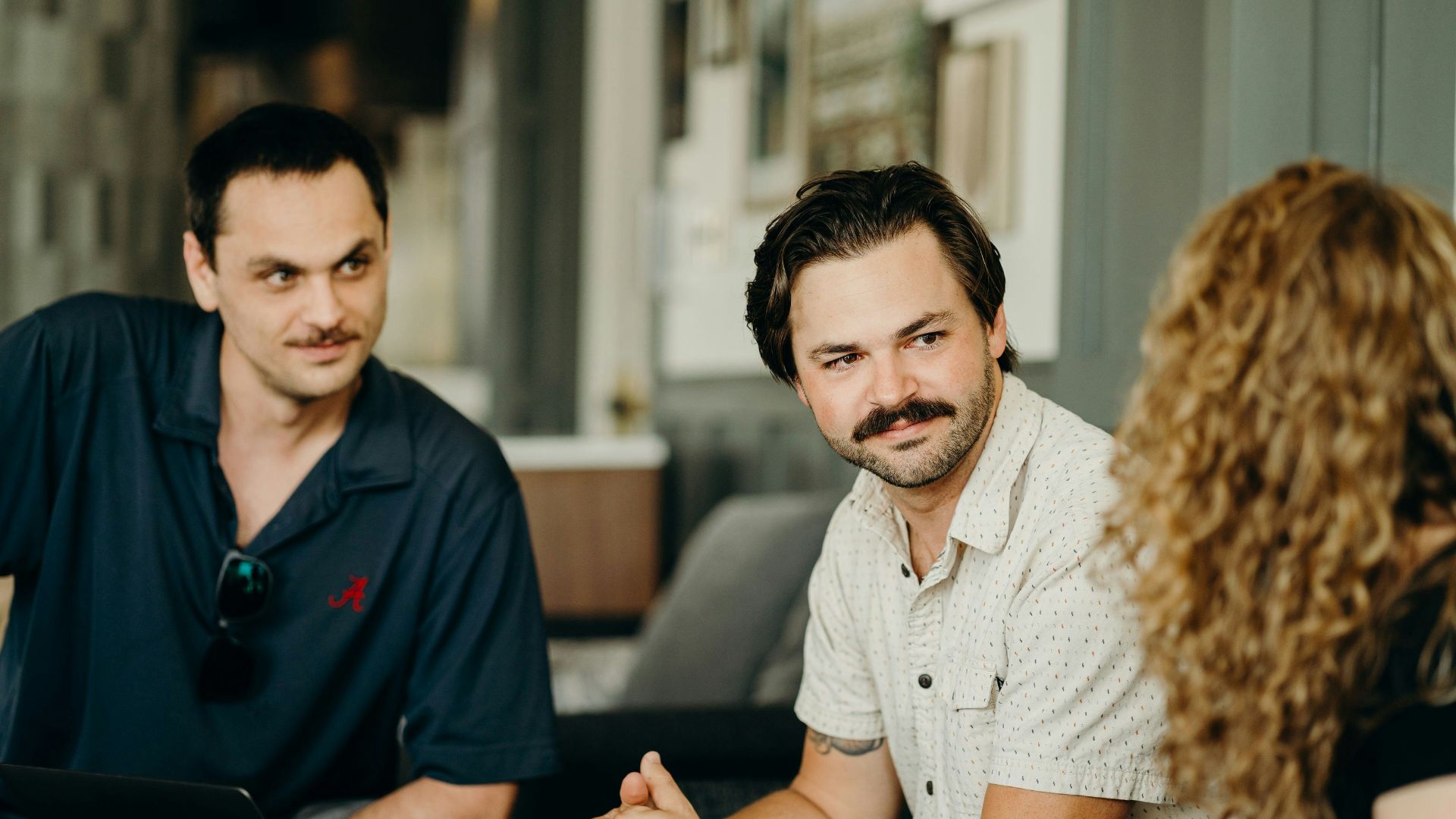 two men and a woman sitting at a table with a laptop