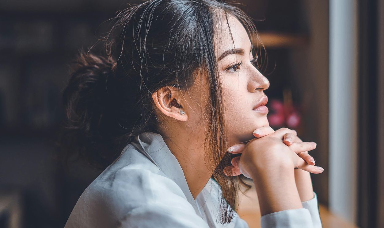 Side profile of a young woman looking out a window, lost in thought, indoors