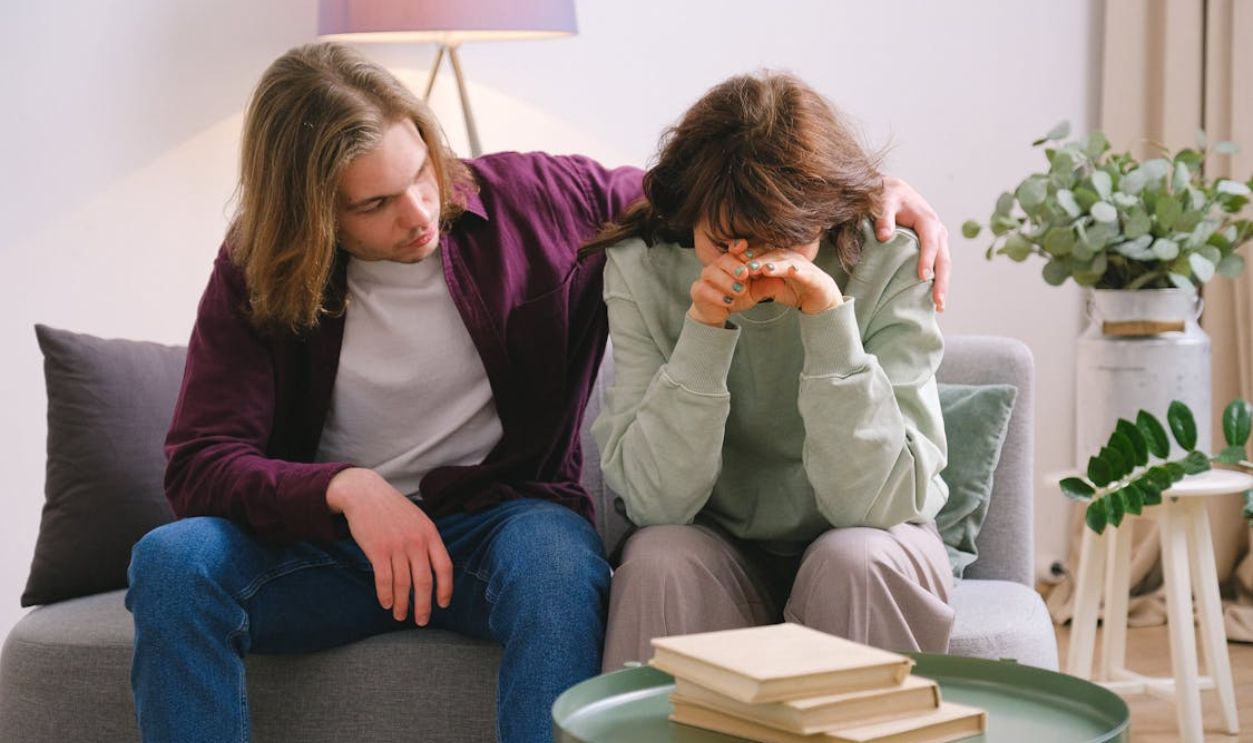 A young couple sitting on a sofa indoors, offering emotional support and comfort
