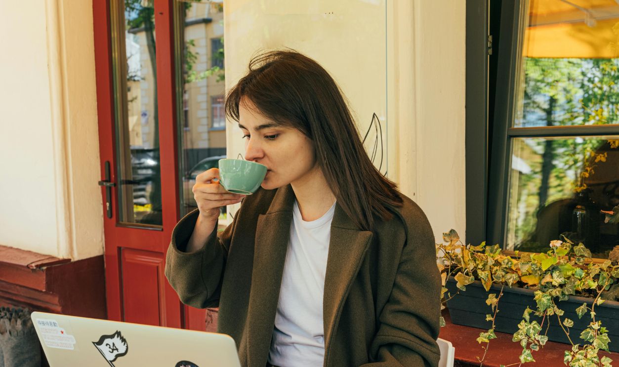Young woman drinking coffee and working on laptop in outdoor cafe setting