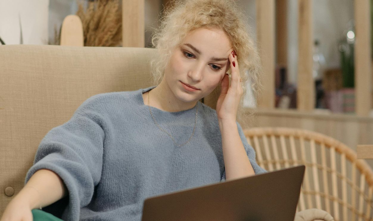 Woman sitting on a sofa with a laptop, enjoying a drink and pastry in a cozy cafe setting