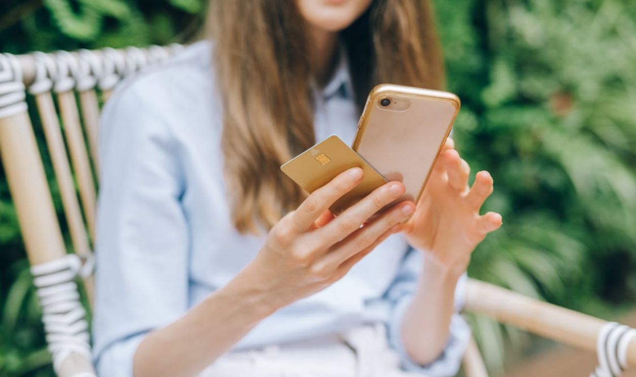 A woman making an online purchase using a smartphone and credit card outdoors