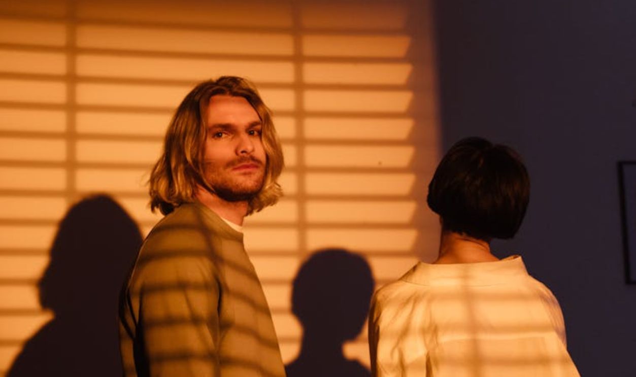 Couple standing indoors with dramatic window blinds shadows, creating a moody ambiance
