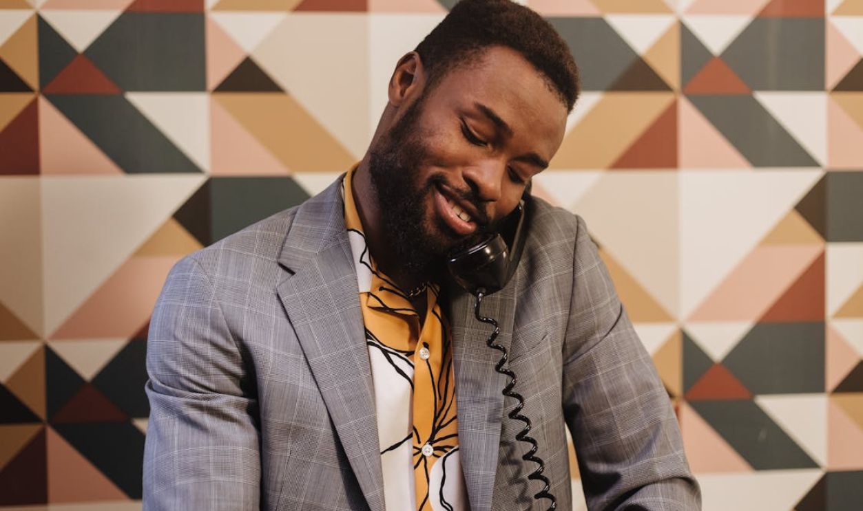 A fashionable man with a beard speaks on a retro telephone in a geometric patterned room