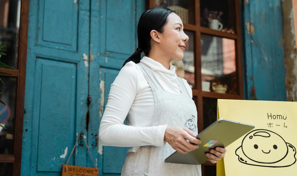 Asian woman with a tablet standing by a rustic blue door with a cute sign