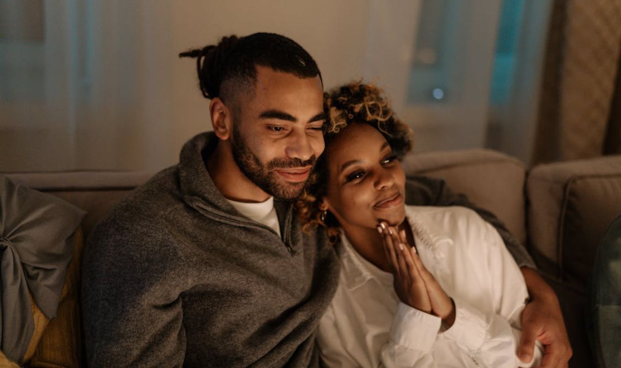 A joyful couple embracing and smiling while sitting on a sofa indoors. Warm and cozy atmosphere.