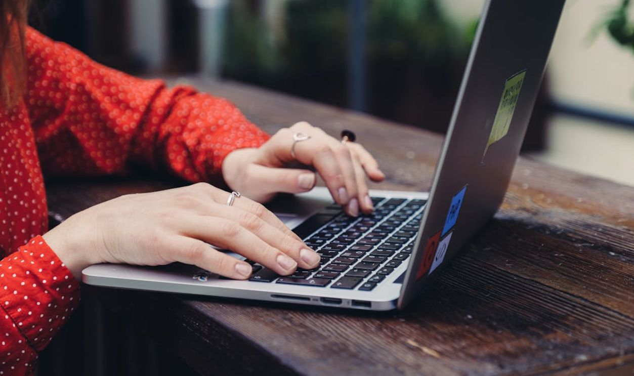 Close-up of hands typing on a laptop placed on a wooden table outdoors