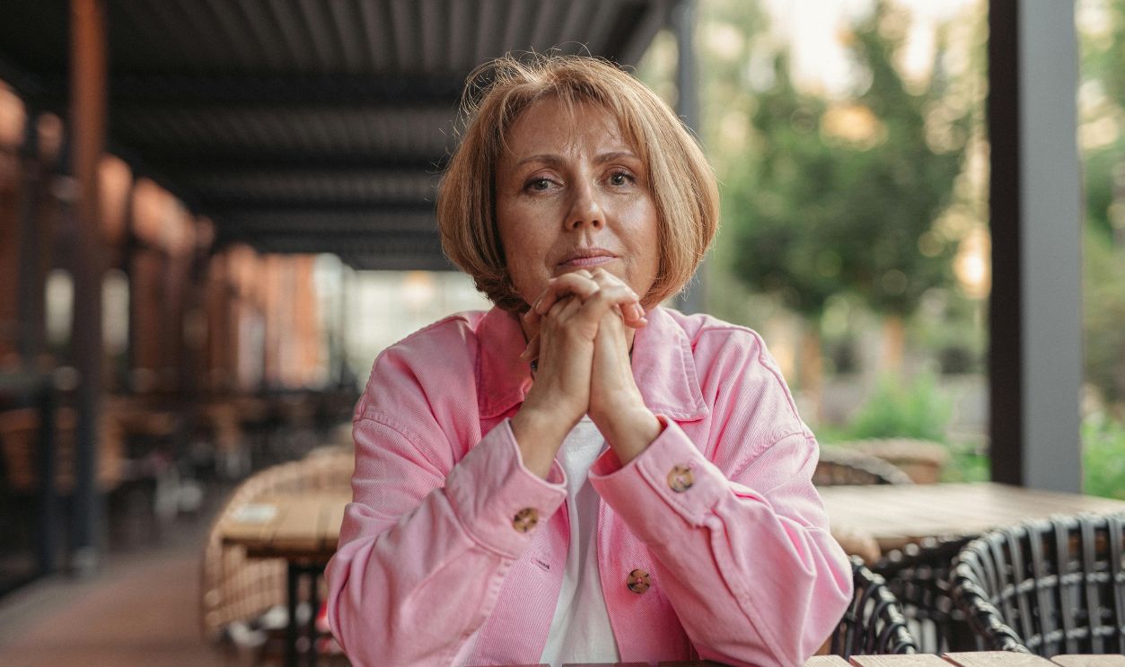 Portrait of a senior woman in pink, sitting outdoors in a contemplative pose