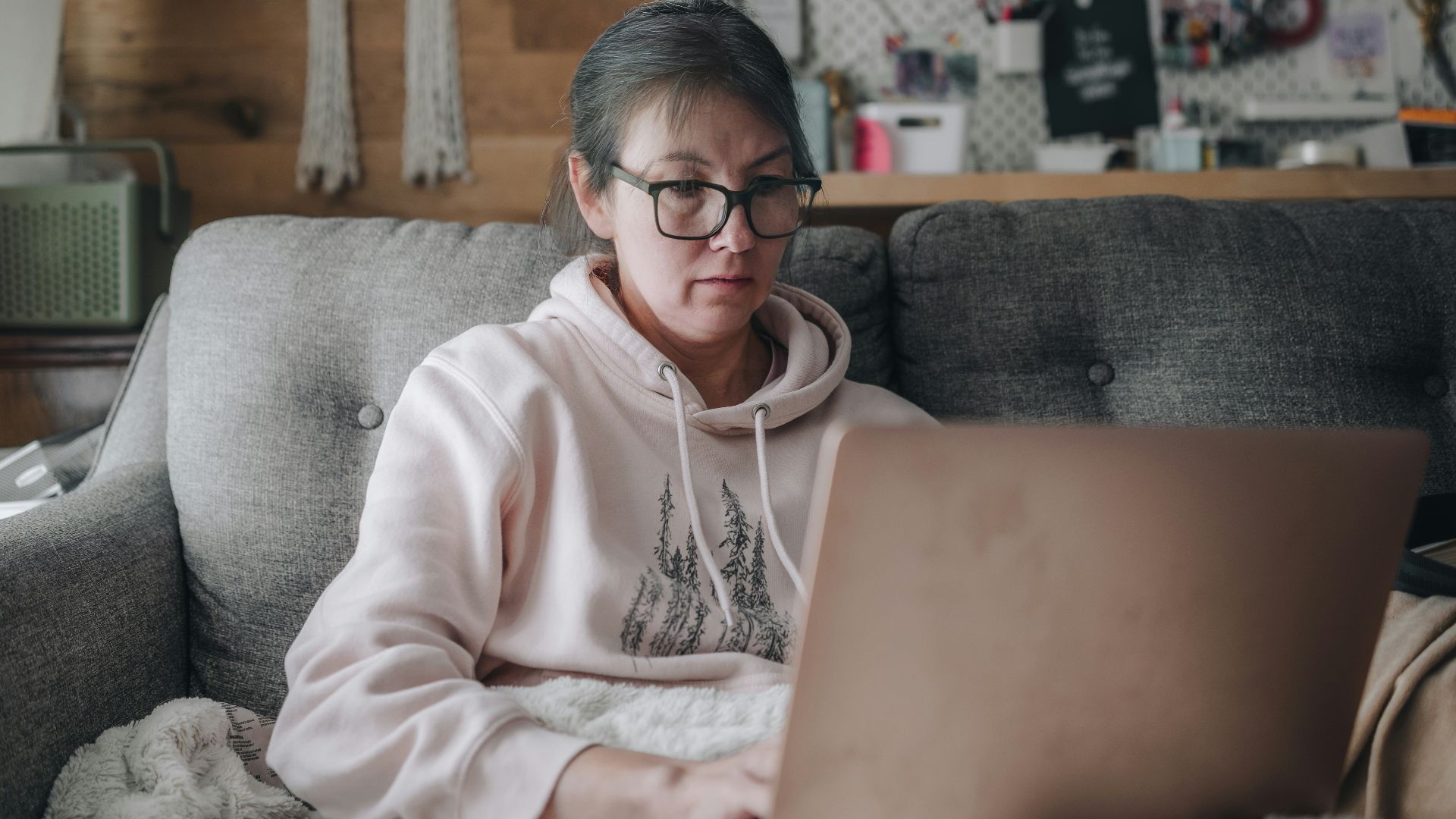 Woman works on laptop while sitting on a couch.