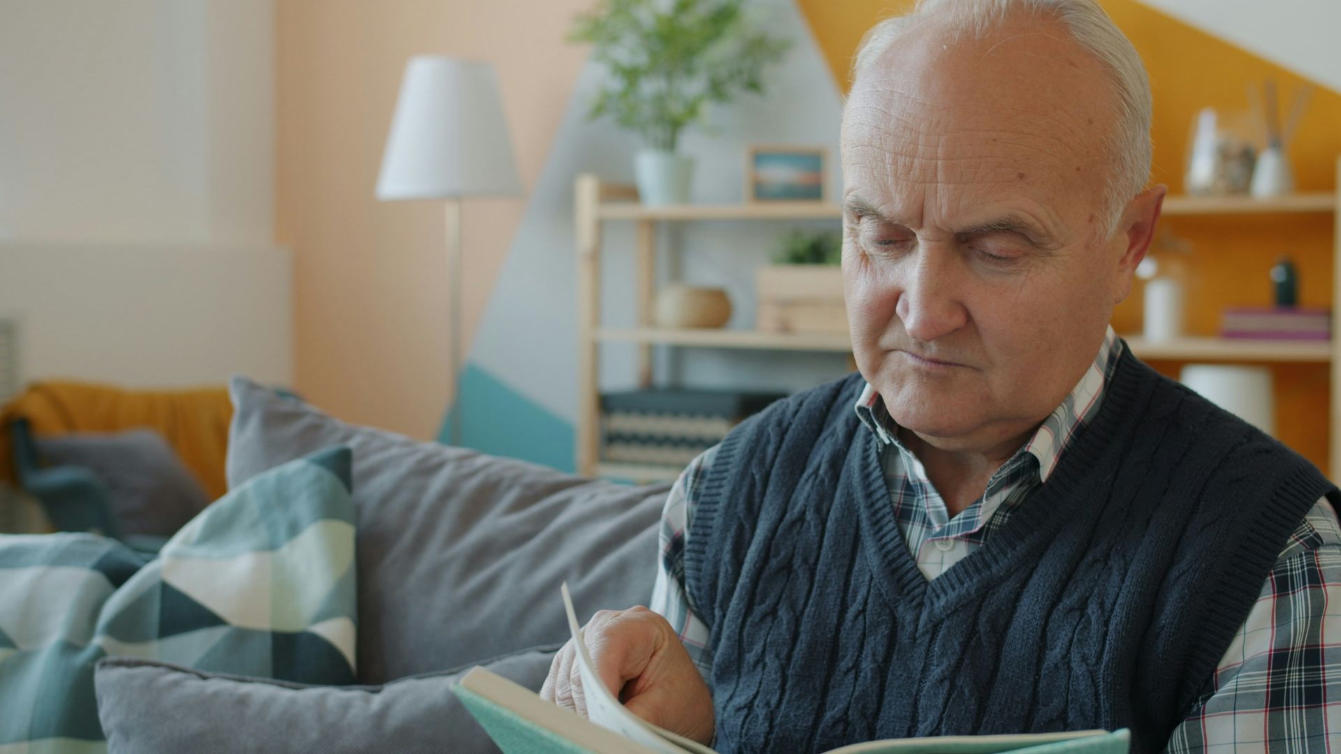 Elderly man reading a book on a couch.