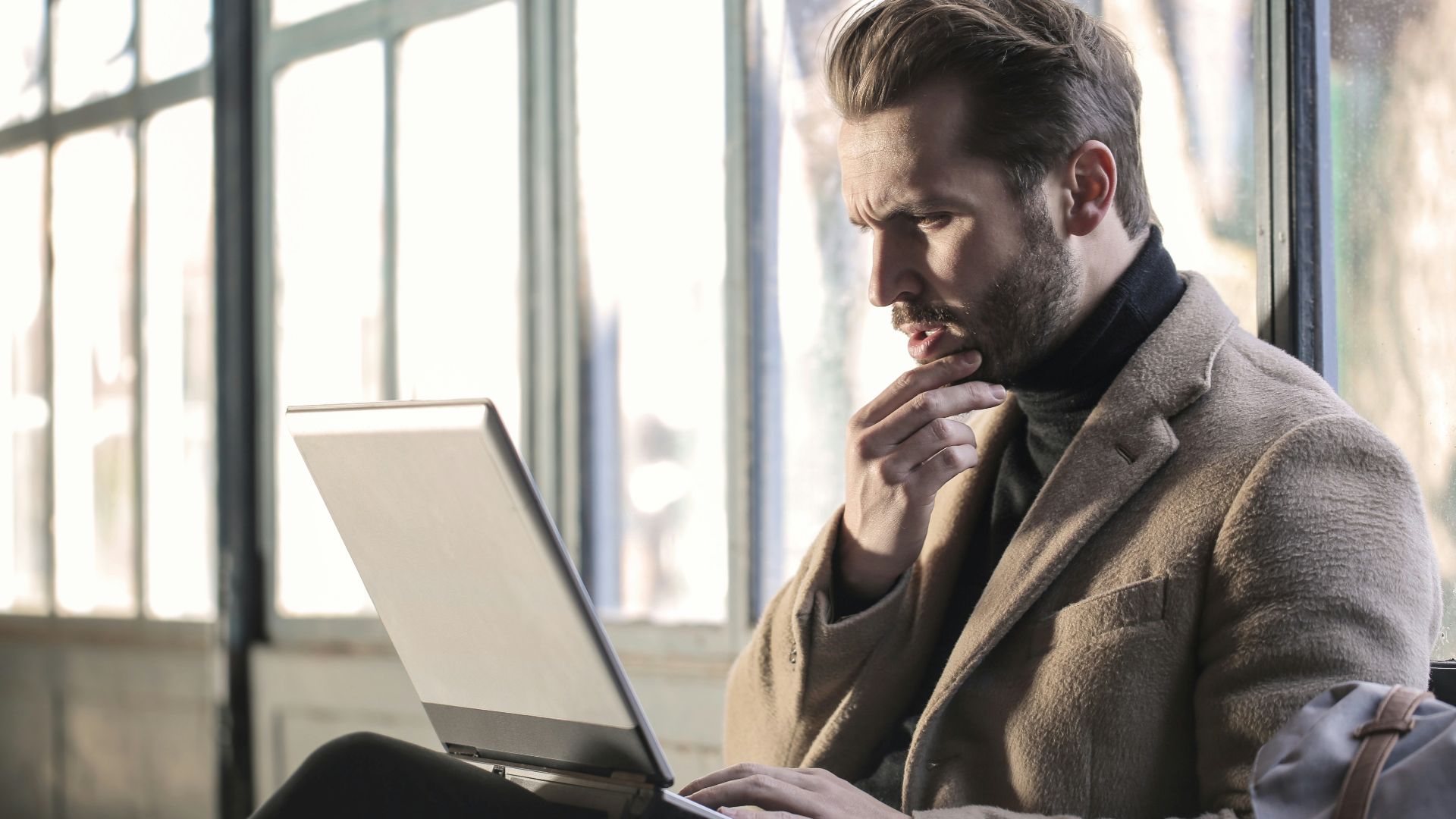 man holding his chin facing laptop computer