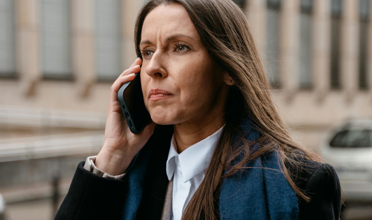 Confident woman in business attire talking on phone while walking in urban setting.