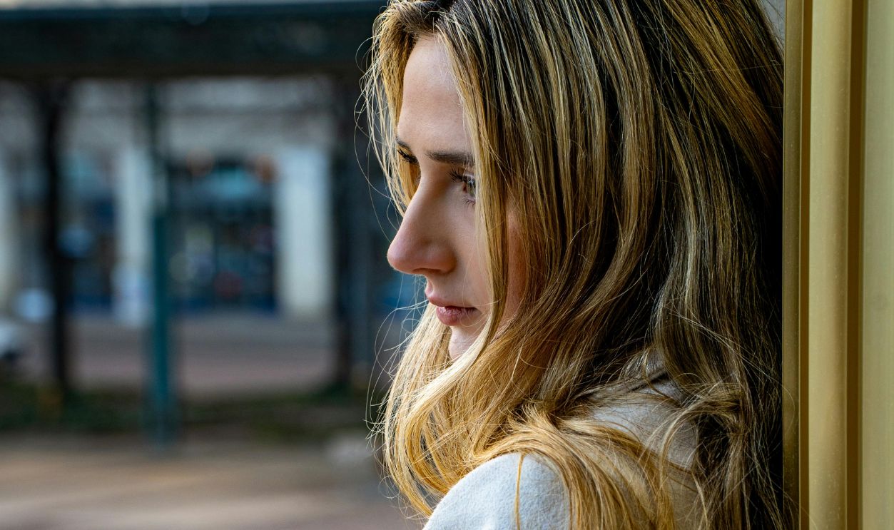 Profile portrait of a woman leaning against a wall in an urban setting, lost in contemplation