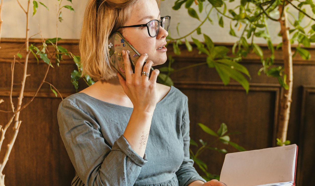 A woman florist uses her smartphone while holding a notebook in a plant shop