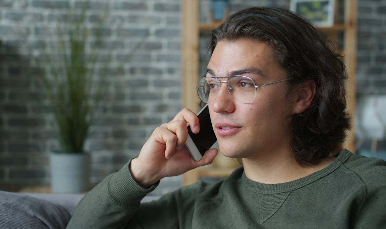 Casual young man talking on smartphone indoors, wearing glasses