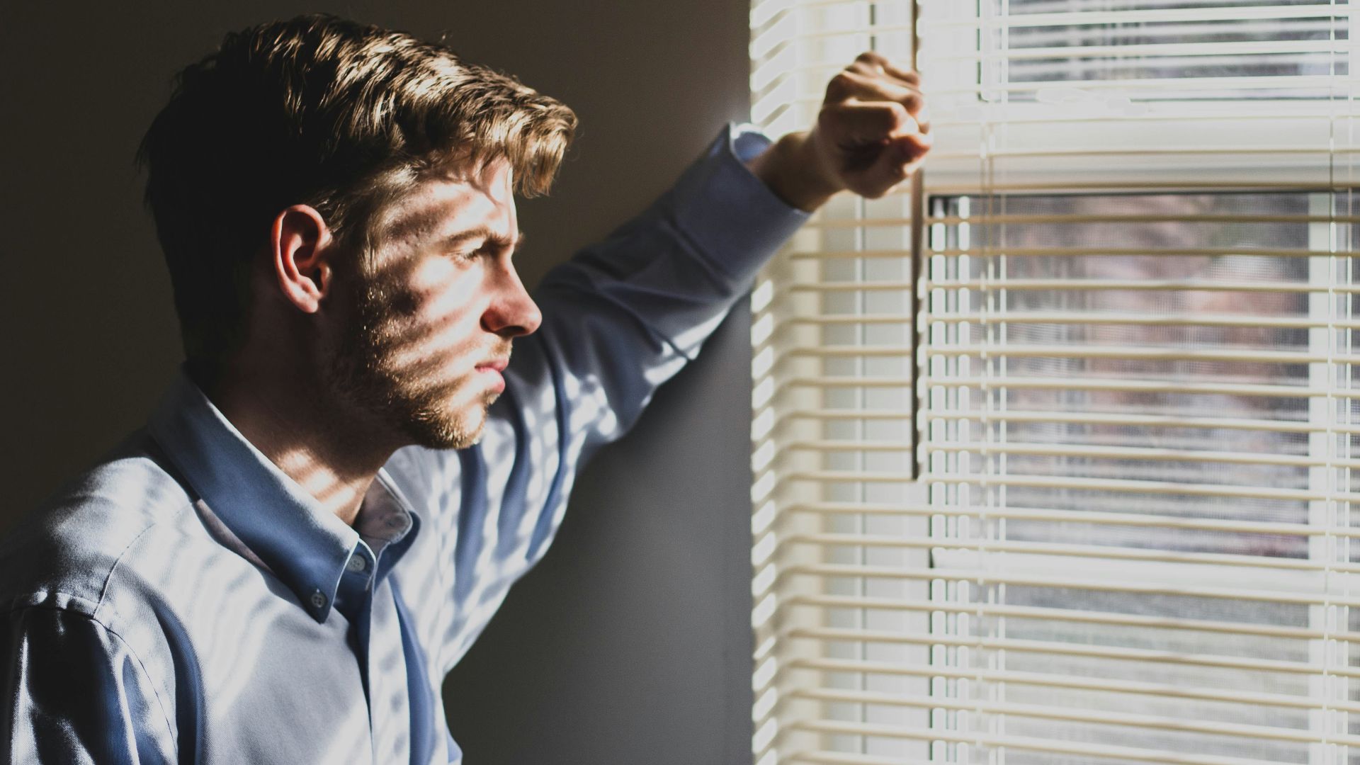 person near clear glass window pane and window blinds low-light photography