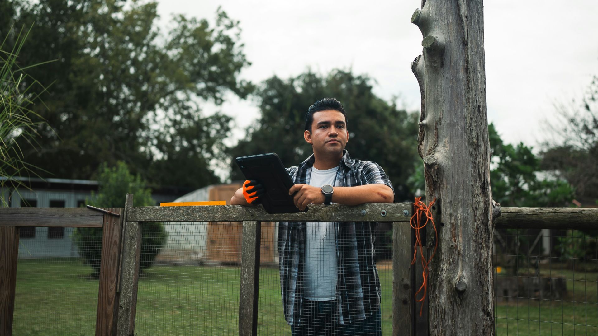 Man holding tablet standing by a wooden fence outdoors