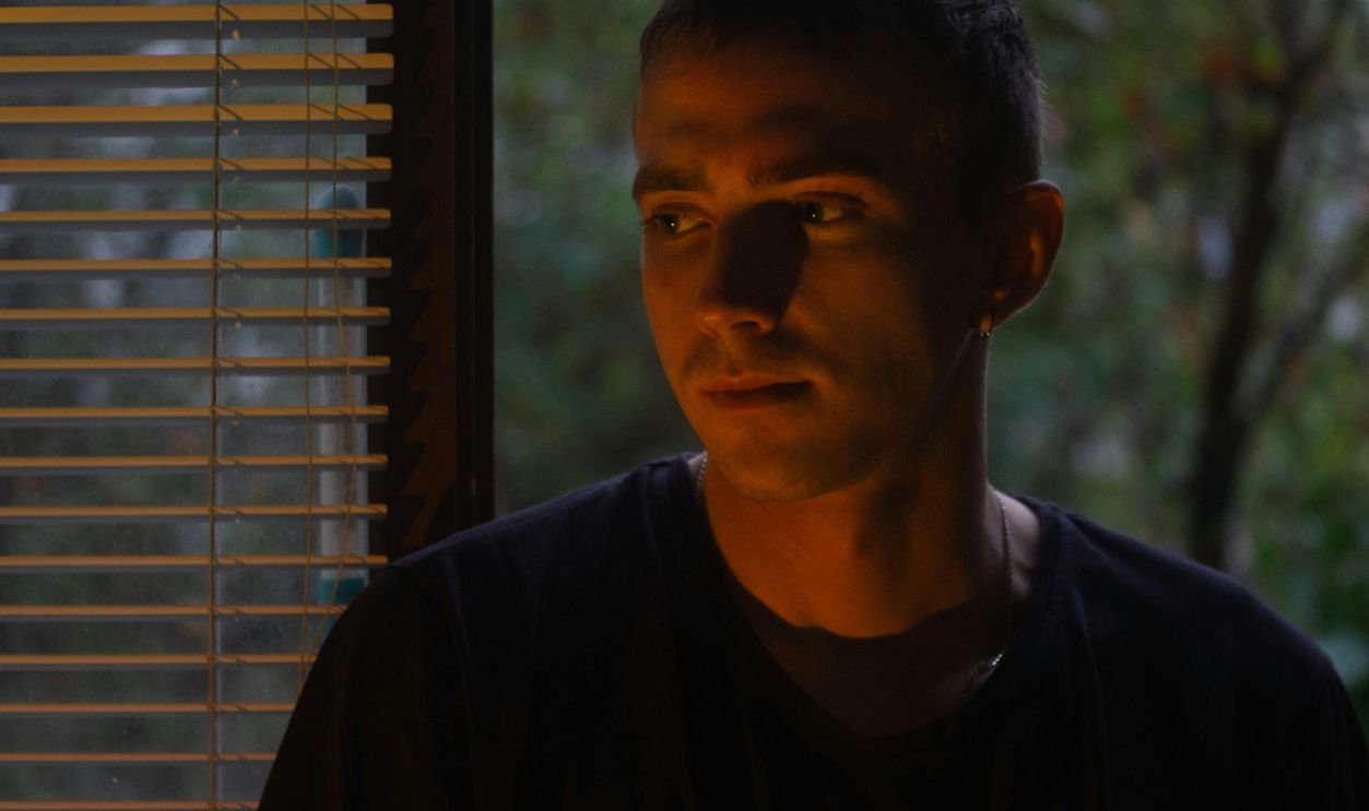 A young man stands by a window, casting dramatic shadows on his face