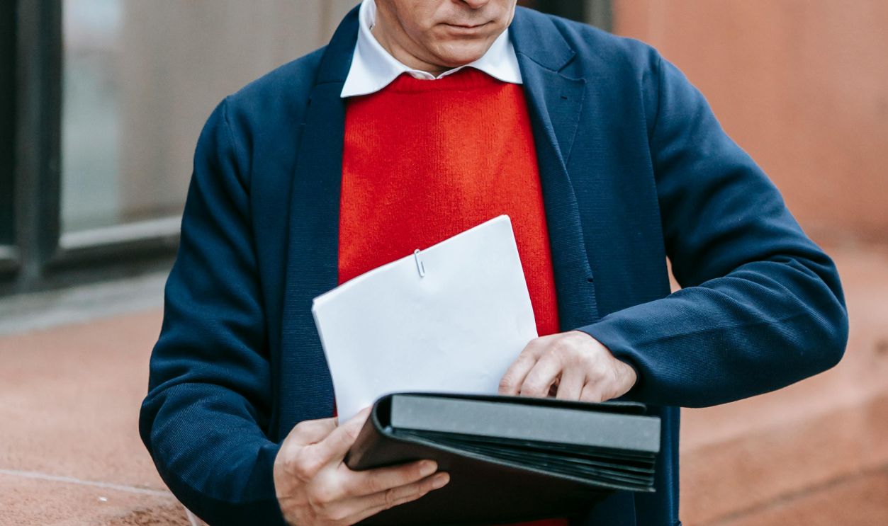 A man dressed in formal attire examines papers outside a building
