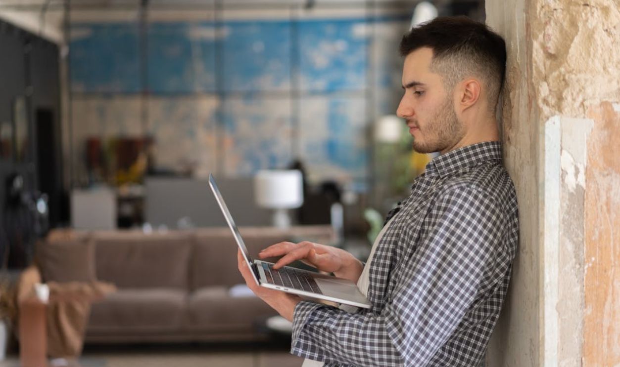 Man working on a laptop standing indoors with a modern office background. Ideal for business and technology themes