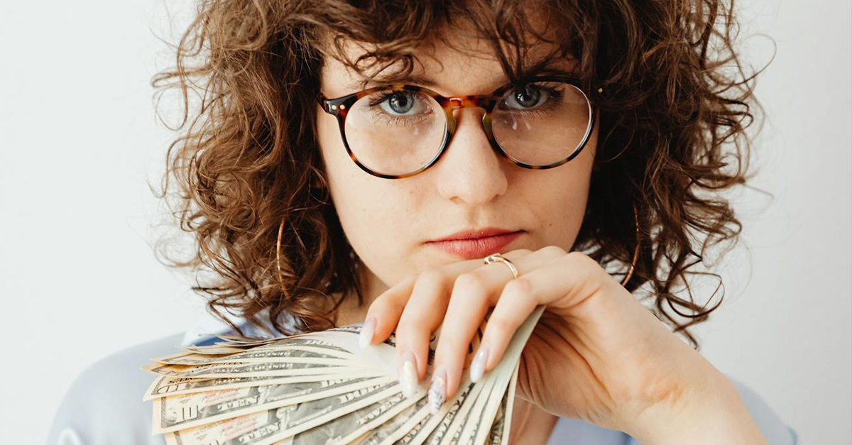 Woman with curly hair and glasses, holding a stack of cash.