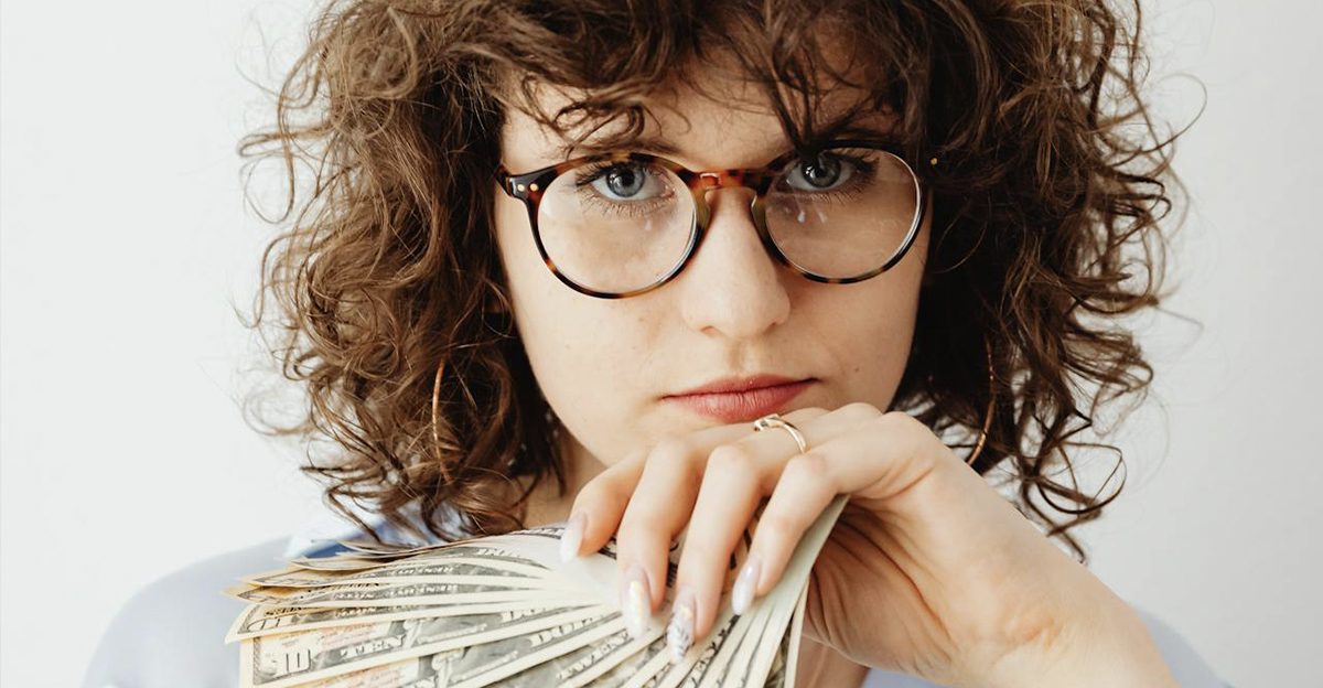 Woman with curly hair and glasses, holding a stack of cash.