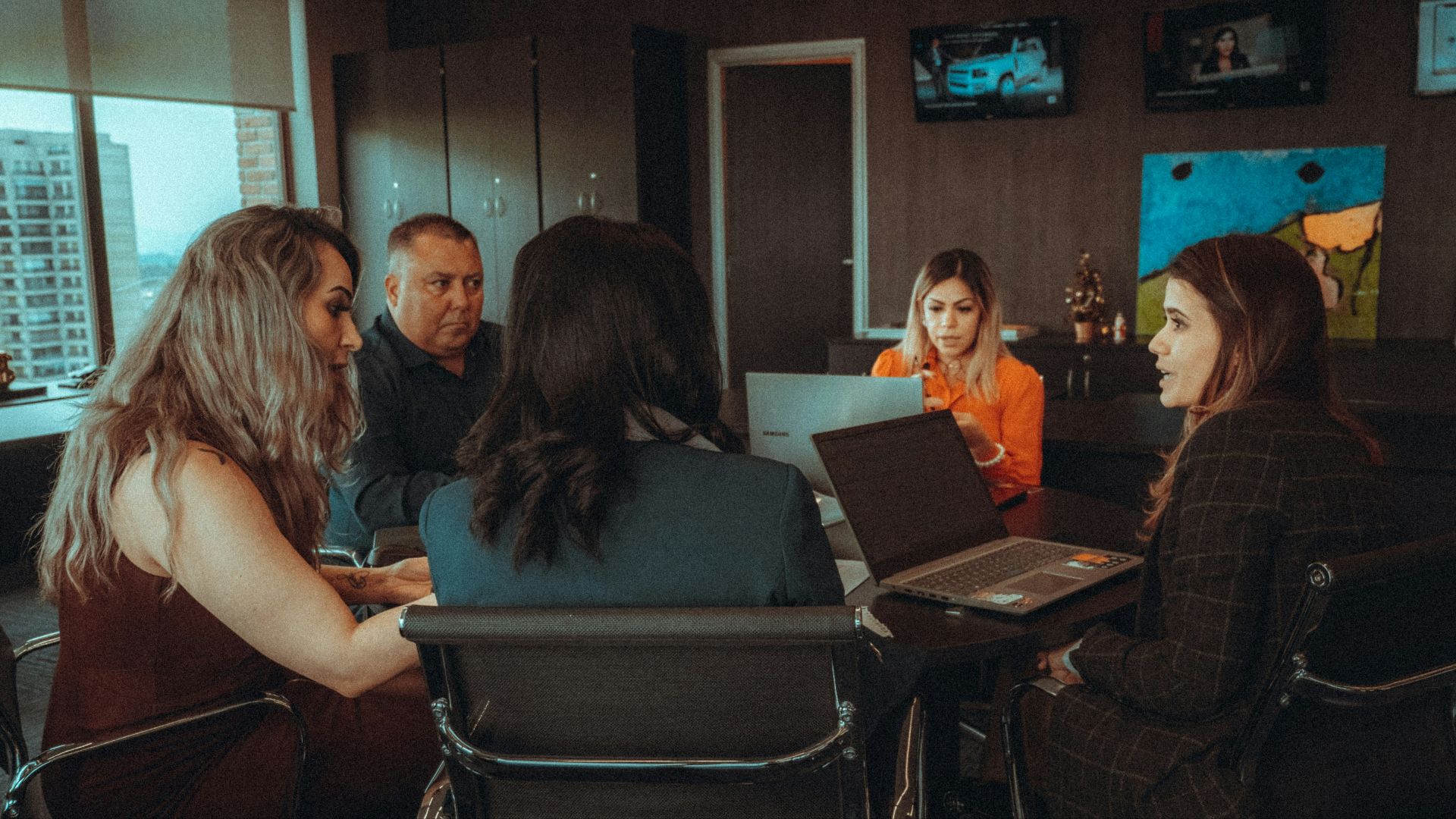 a group of people sitting around a table with laptops