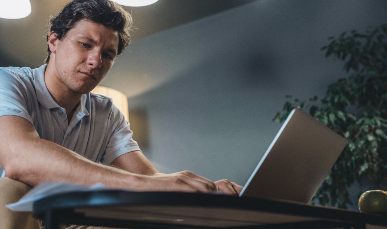 Adult man concentrating while working on a laptop indoors, in a modern office setting.